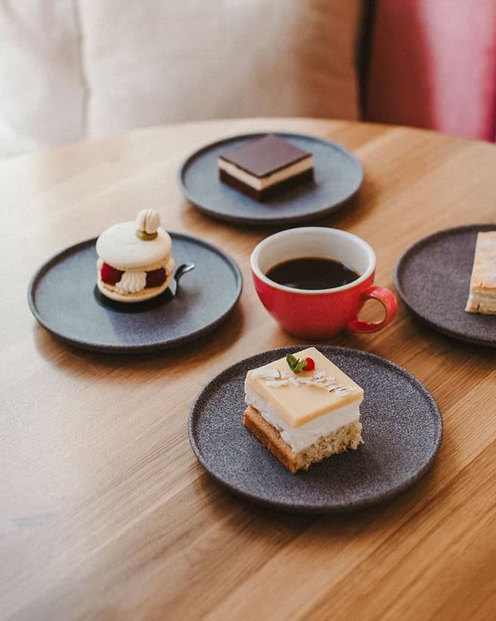 four vegan desserts on individual plates with a black coffee in the center on a wood table at share sweets in prague