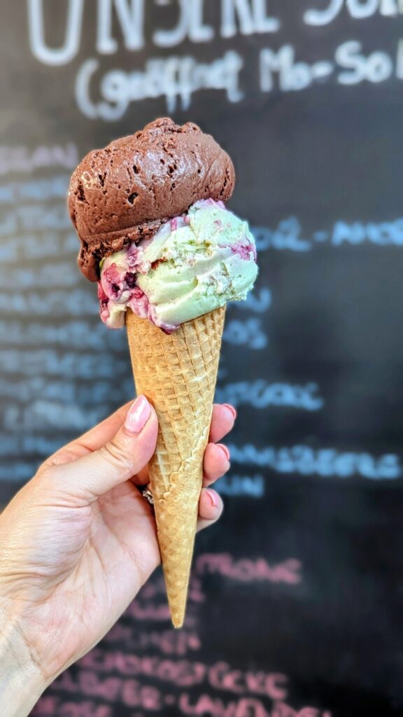 a vegan ice cream cone with a scoop of light green and purple ice cream and dark chocolate