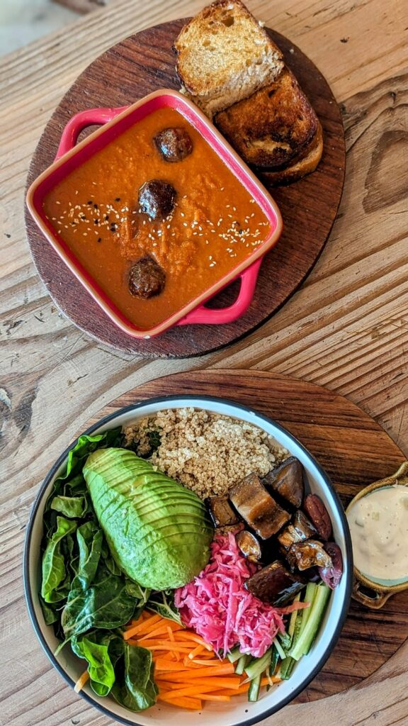 overhead shot of a colorful bowl of fresh veggies next to a grilled cheese sandwich on a wood platter with a bowl of tomato soup the Conscious Kitchen in cape town 