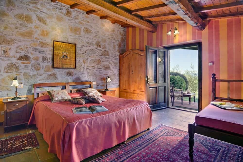 inside of a rustic guestroom with light wood ceiling beams, stone walls, and dark bedding at the vegan friendly Montali Country House in italy