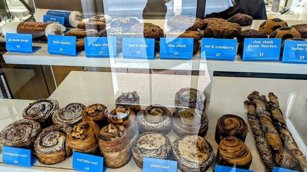 a dessert and pastry case filled with rows of golden vegan pastries all in a row at  okja in cape town