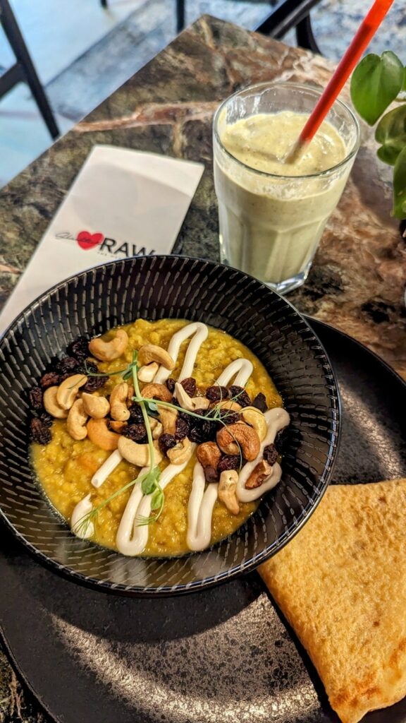 a bowl of spiced kitchari in a black bowl next to a green smoothie on a dark table at Scheckters Raw  in cape town