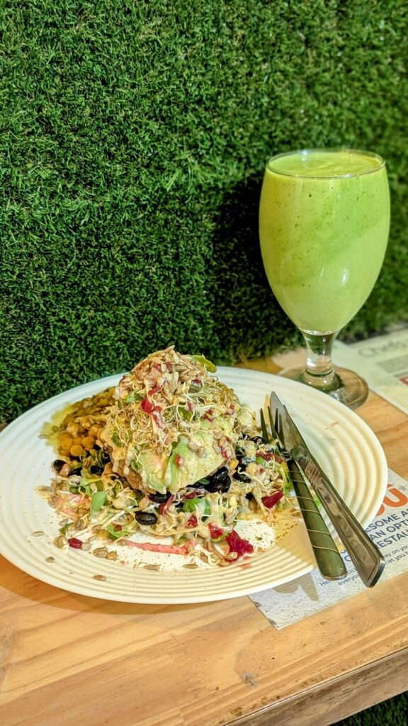 a vegan burger topped with a mound of fresh micro greens and sprouts next to a green smoothie at Sunshine Food Sprouting in cape town