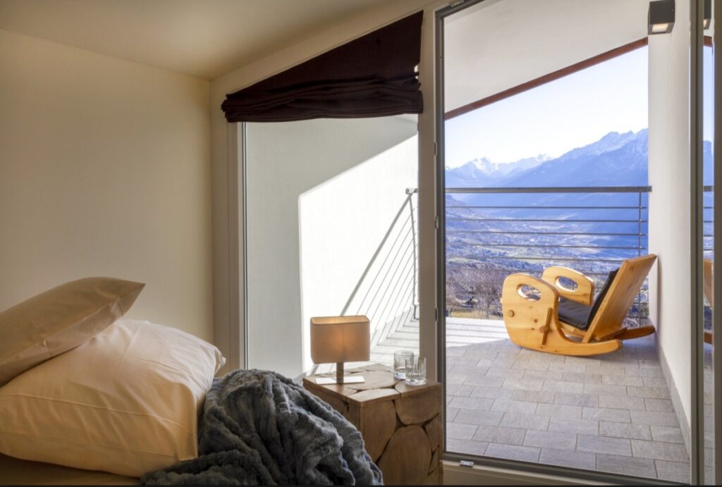 guest room with a balcony that overlooks the mountains at the vegan inn hirondelle in italy