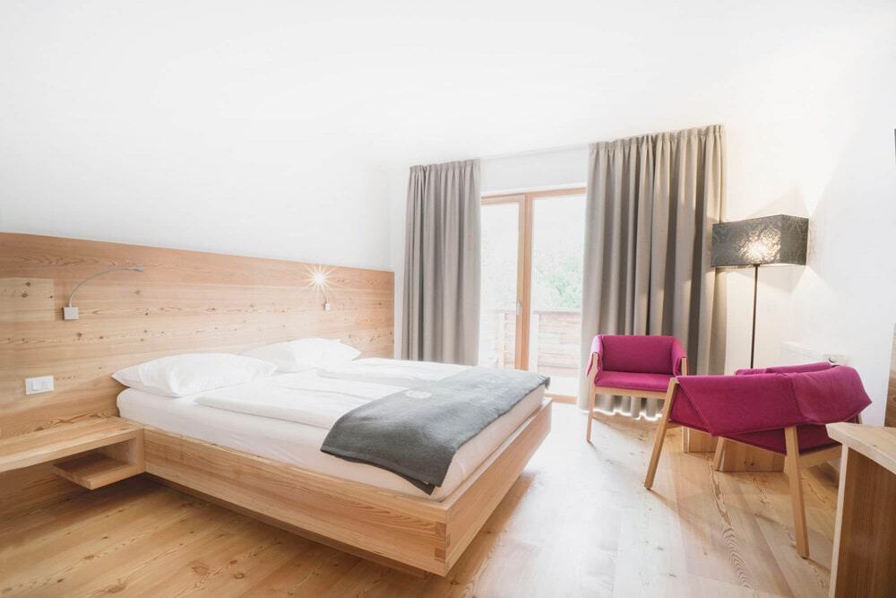 a modern and bright guest room with a light wood floor and bed frame and large window at the vegan hotel la vimea in italy