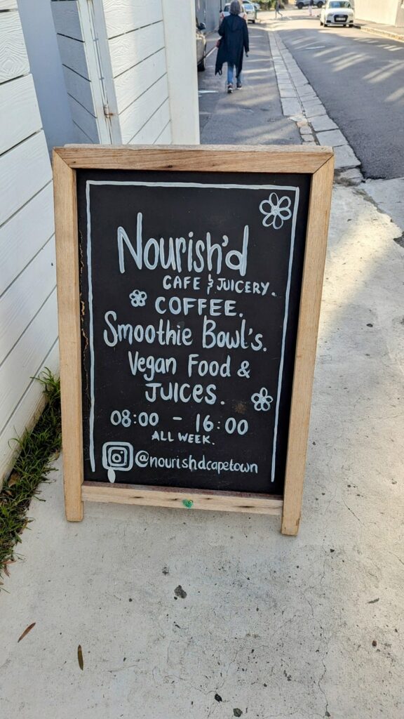 a black chalk board promoting the vegan cafe nourish'd outside their green point location in cape town