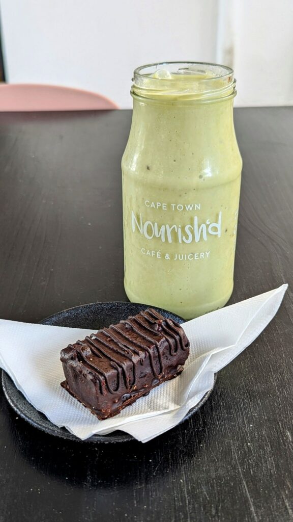 a small vegan and raw snickers bar on a white napkin next to a large green smoothie at nourish'd in cape town