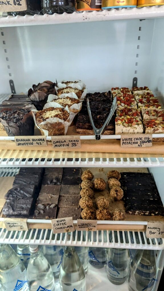 two shelves of vegan and raw desserts in side of a cooler at nude foods in cape town