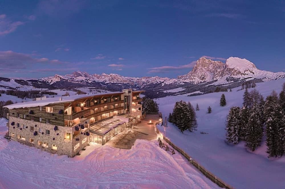 the vegan hotel paradiso pure living covered in snow at night time with a light golden glow from the outdoors lights and snowcapped mountains in the distance