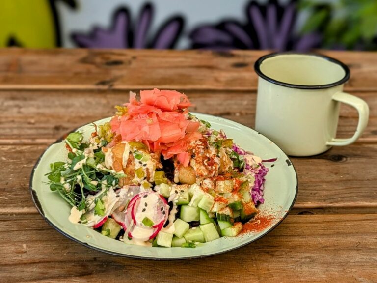 a colorful vegan rice bowl with tempura cauliflower and fresh pickled ginger next to a light green mug on a picnic table at wild eatery in cape town