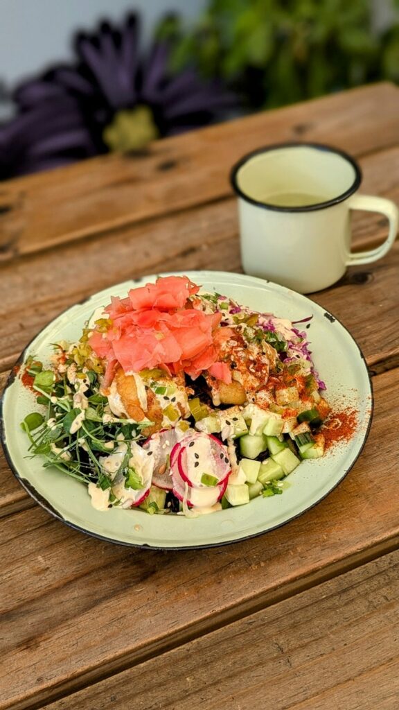 a colorful vegan rice bowl with tempura cauliflower and fresh pickled ginger next to a light green mug on a picnic table at wild eatery in cape town