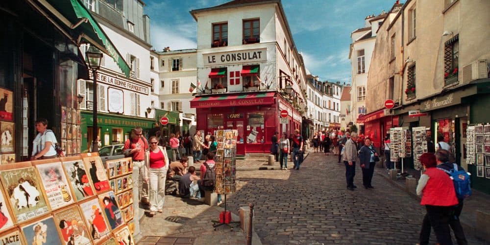 a quintessential neighborhood in paris with small cafes and a book shop with books on the sidewalk and a few people passing through