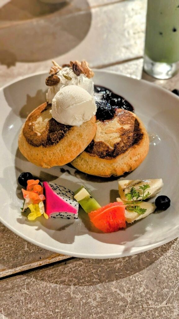 two small fluffy vegan souffle pancakes topped with a scoop of vanilla ice cream and fruits at ain soph in kyoto