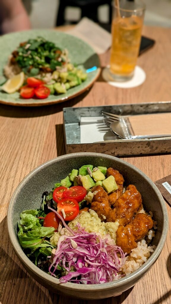 a bowl of vegan karaage in front of a bowl of vegan curry on a dining table at cosme kitchen tokyo