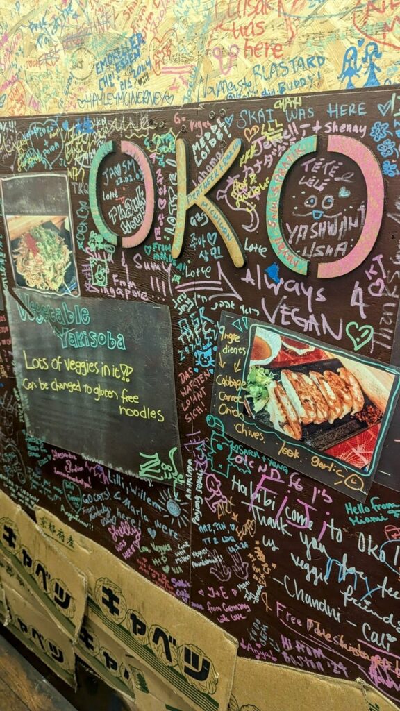 a black chalk board covered in colorful writing on a yellow wall with the headline OKO at OKO-Fun Okonomiyaki Bar 