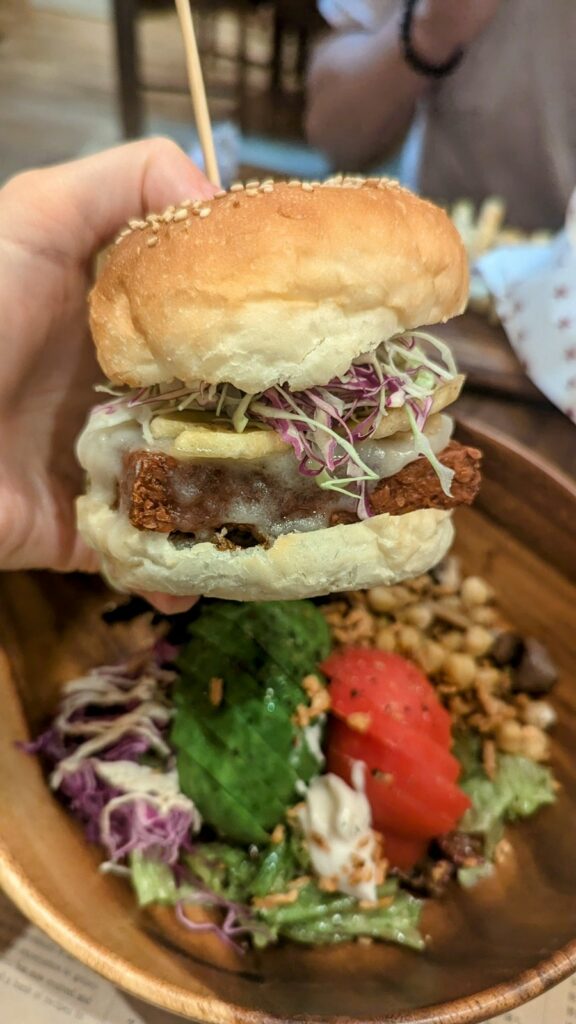 a vegan burger with cheese and sprouts coming out of the middle held over a salad at Premarché Alternative Diner in kyoto