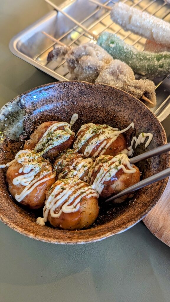 a small round bowl of vegan takoyaki covered with a small amount of white cream sauce with chopsticks off to the side at Shinsekai Paprika Shokudo osaka