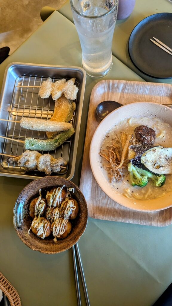 overhead view of vegan ramen, takoyaki, and fried skewered veggies on a wood table at Shinsekai Paprika Shokudo in osaka