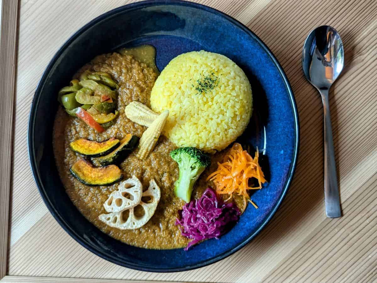 a large bowl of vegan curry with a mound of bright yellow tumeric rice, topped with sliced veggies on a wood tray at the vegan restaurant cafe tea terrace in kyoto