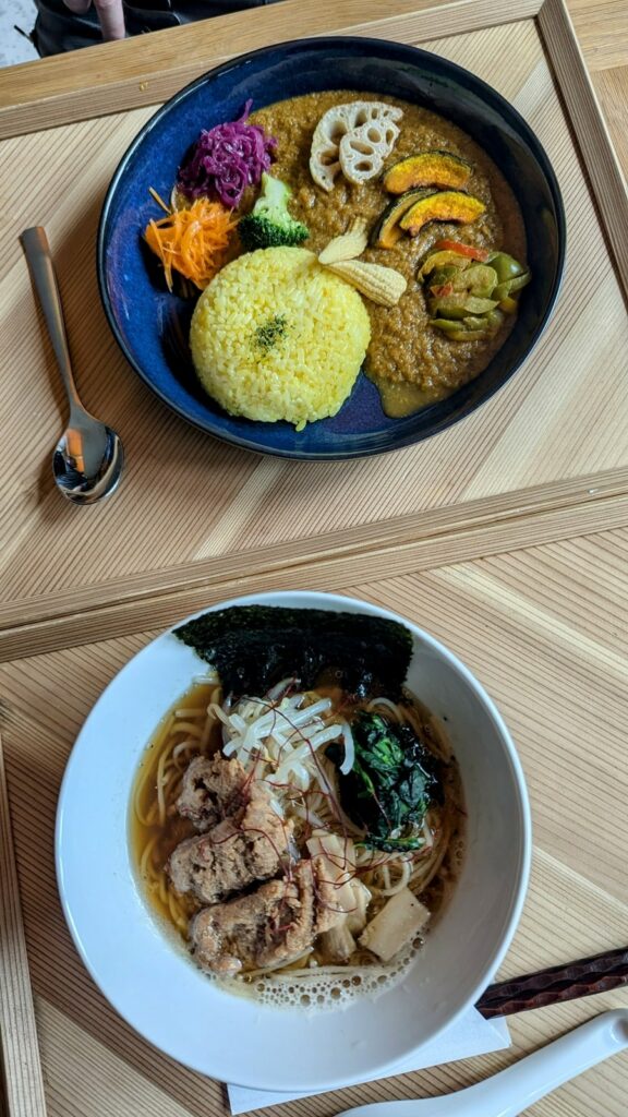 overhead view of a bowl of vegan curry with bright yellow tumeric rice and a bowl of vegan ramen on wood trays at cafe tea terrace in kyoto