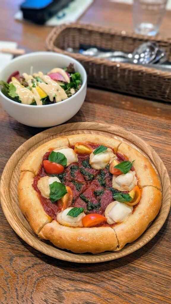 a small round vegan and gluten free pizza next to a small salad on a wood table at choice vegan restaurant in kyoto