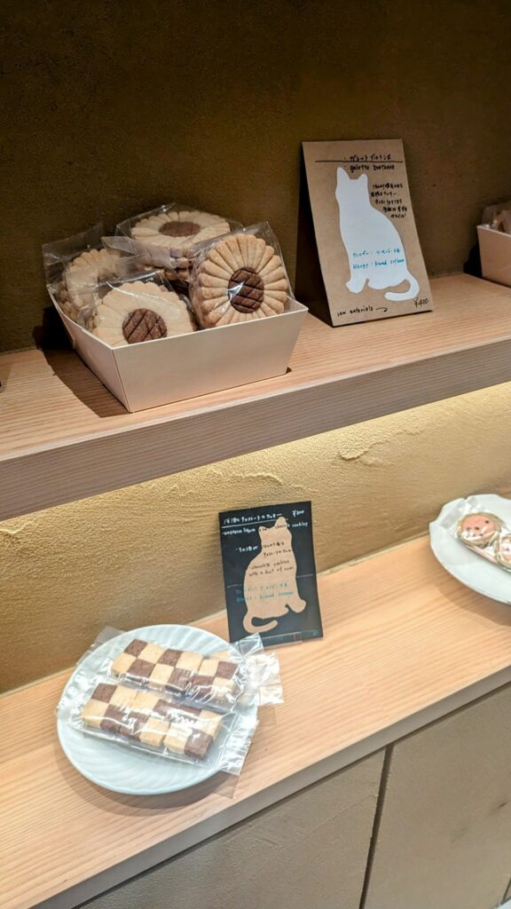 two wood shelves with baskets and a white dish filled with small vegan and gluten free cookies next to small pictures of cakes at naki vegan sweets in osaka