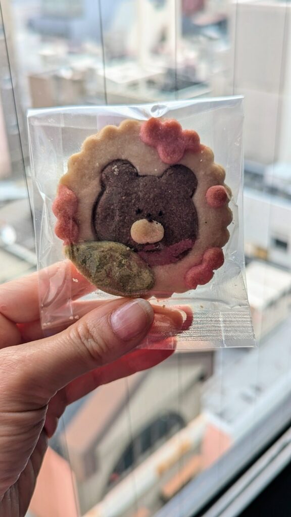 a round vegan and gluten free short bread cookie with a picture of a brown bear in the middle and the edges covered with pink flowers at naki vegan sweets