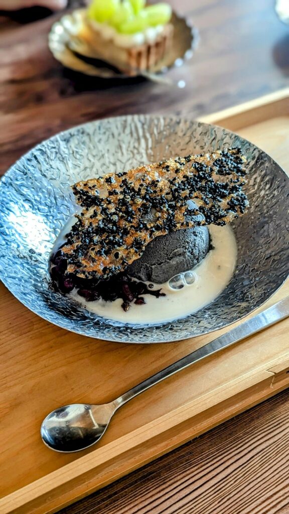 a metallic colored bowl with a single scoop of black sesame gelato in a pool of white cream and topped with a think slice of vegan sesame brittle at onwa in nara