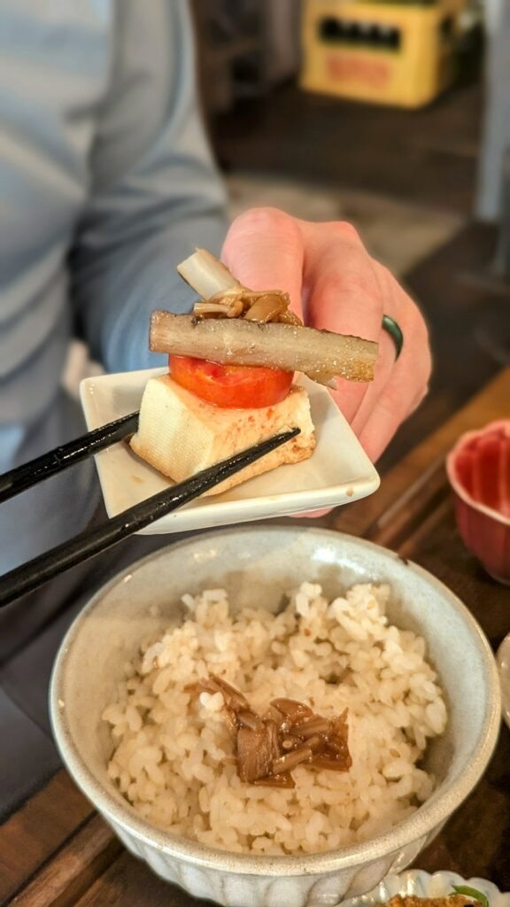 a small rectangle white dish with a piece of tofu topped with mushroom held above a bowl of rice at padma in kyoto