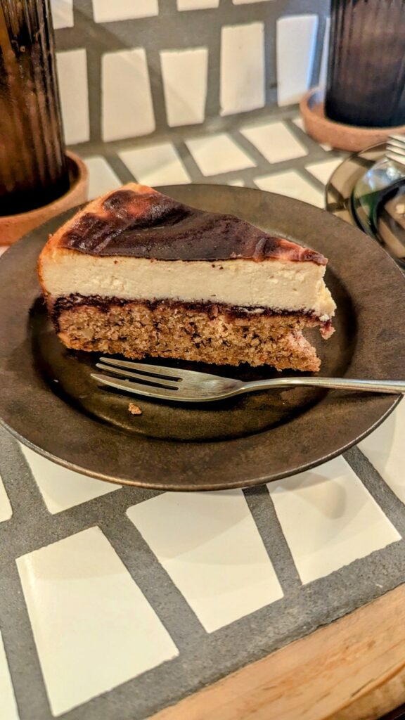 a slice of baked vegan cheese cake with a nut cake base and a thin layer of plum jam on a white tile counter at re public by base island kitchen