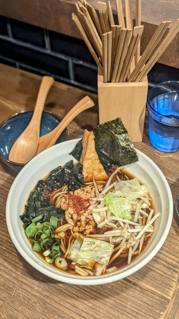 a bowl of vegan ramen with a chunk of fried tofu and seaweed on top next to a container with a bunch of wooden chopsticks at vegan playpen in osaka