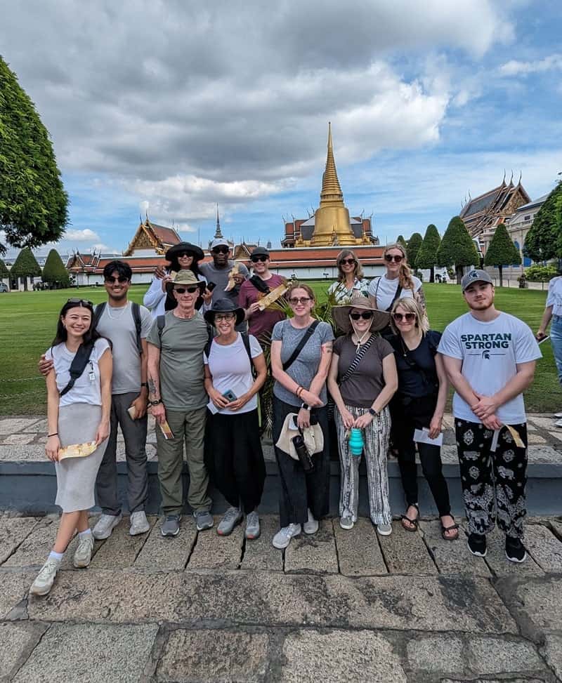 a group of 15 people standing in front of the grand palace in bangkok during a veggies abroad vegan tour to thailand