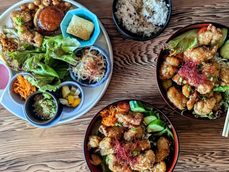 two bowls filled with golden vegan fried chick'n pieces with a little bit of greenery next to a larger round platter filled with little dishes of sauce and colorful veggies on a wood table at onwa in nara