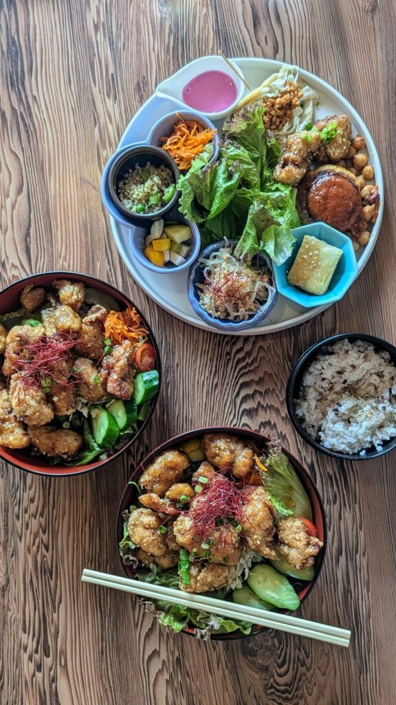 two small bowls of crispy vegan kaarage next to a large round plate with colorful vegetables on a wood table at a vegan restaurant in nara, japan