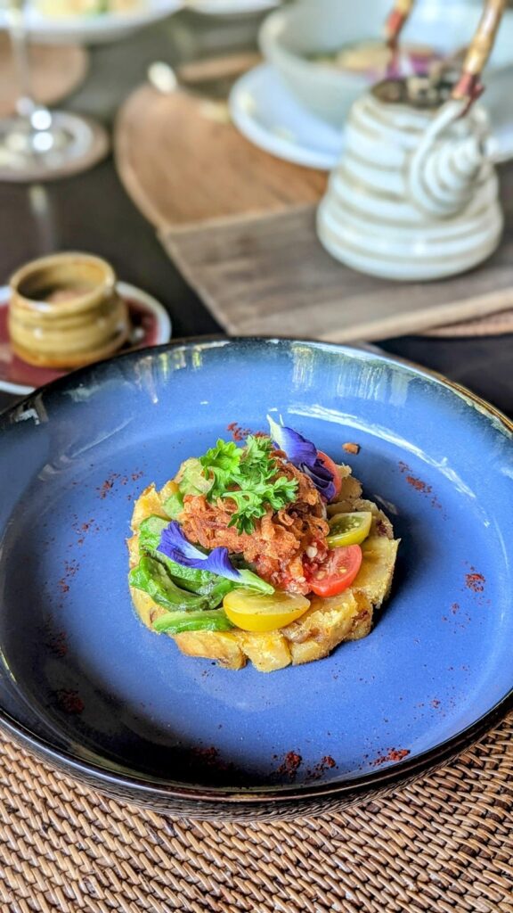 a round sweet potato hash topped with edible flowers and crispy onions on a blue plate at fivelements retreat in bali