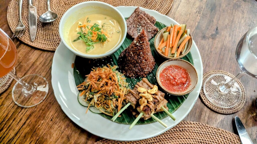 a vegan Balinese platter with a pyramid of rice next to tempeh satay, salad, pickled veggies and sauces in small bowls on a wood table at fivelements retreat in ubud, bali 