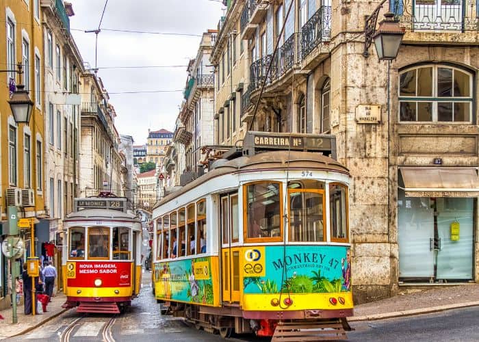 two colorful antique tram cars coming up a narrow street in lisbon