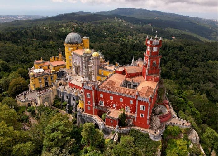 overhead view of the brightly colored pena palace sitting on top of a lush green hill in sintra