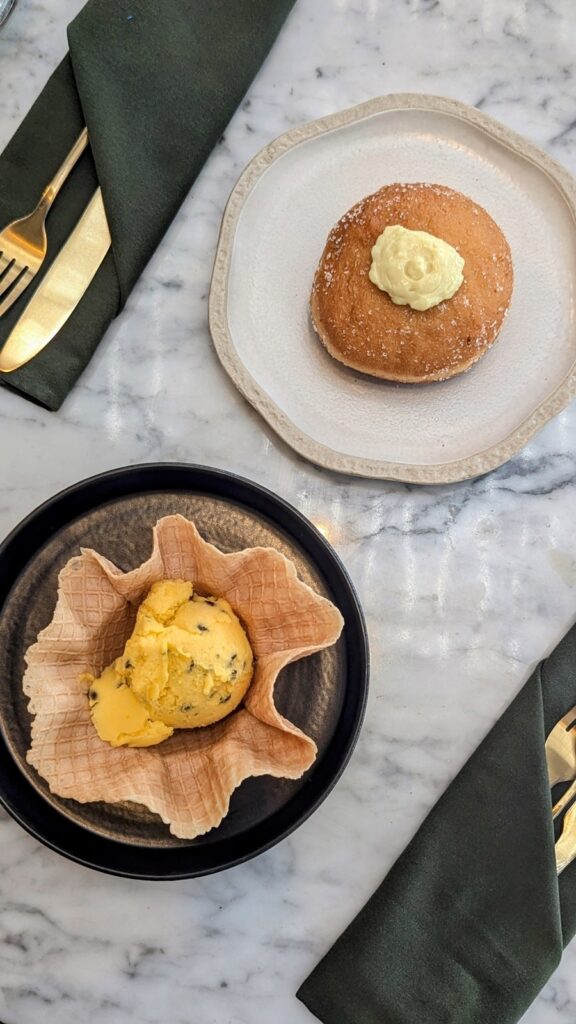 a vegan waffle cone bowl with a single scoop of yellow passionfruit gelato next to a golden vegan donut filled with cream on a marble table at plant bistro in ubud