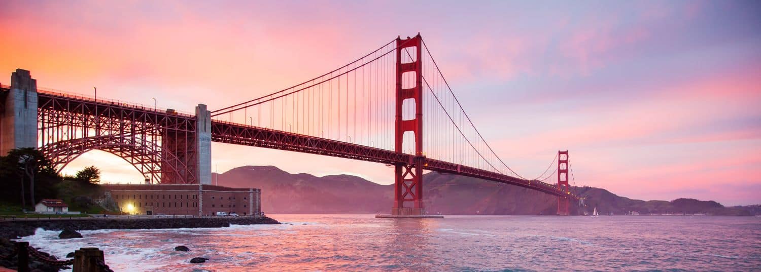 the golden gate bridge in front of a purple and pink sky as the sun sets over San Francisco