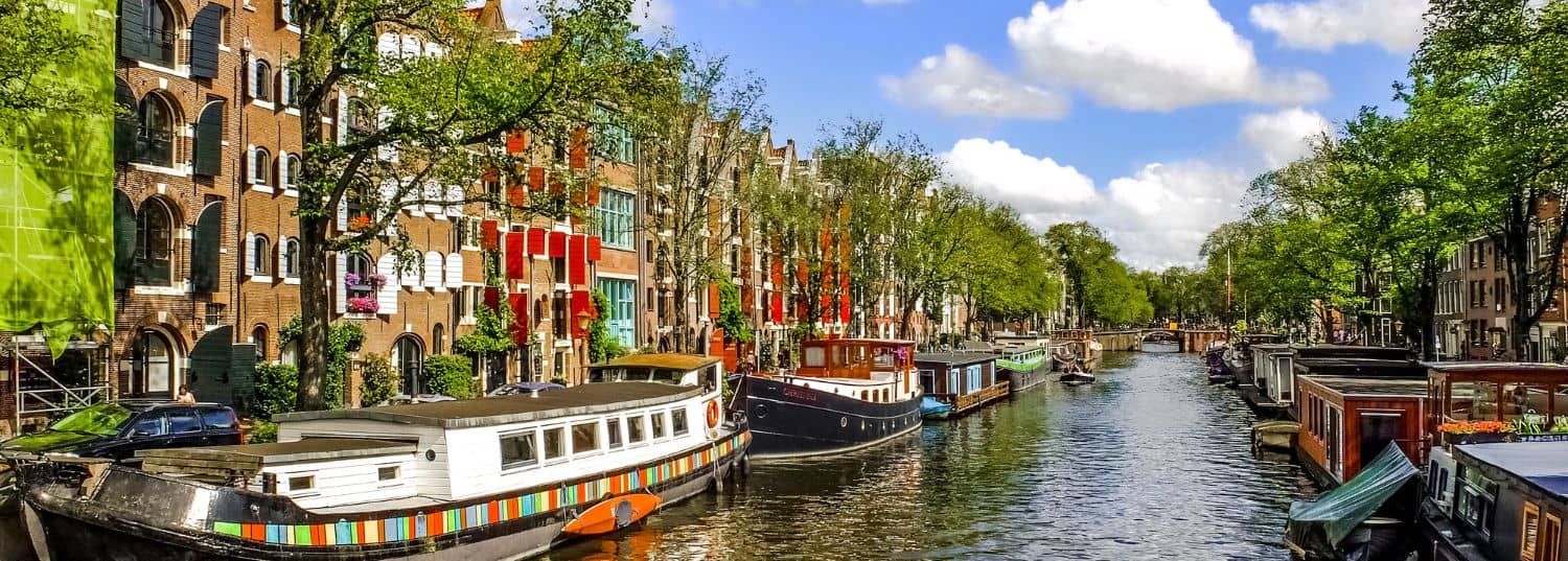 a quiet canal in amsterdam with house boats parked off to the side on a bright, sunny day