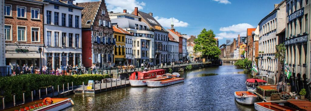 charming canal with a few boats anchored to the side surrounded by old world buildings in belgium