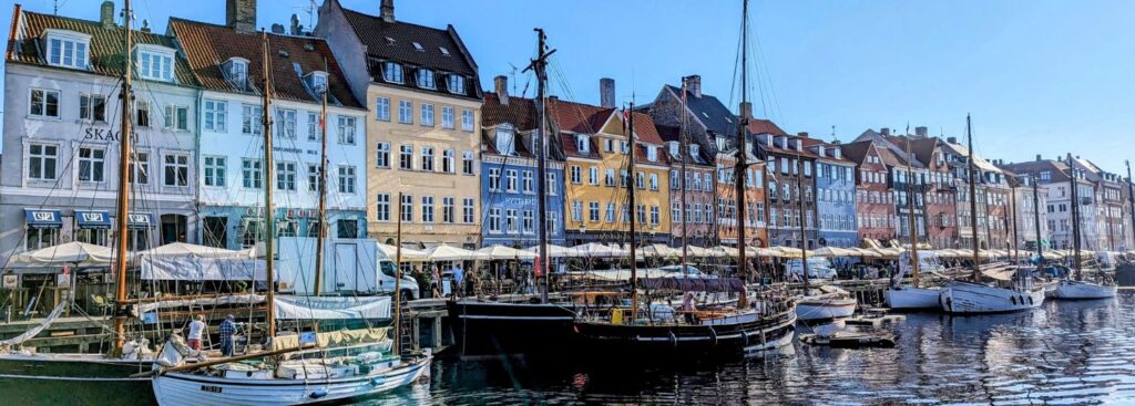 sail boats sitting in the harbor in front of a row of colorful houses in copenhagen