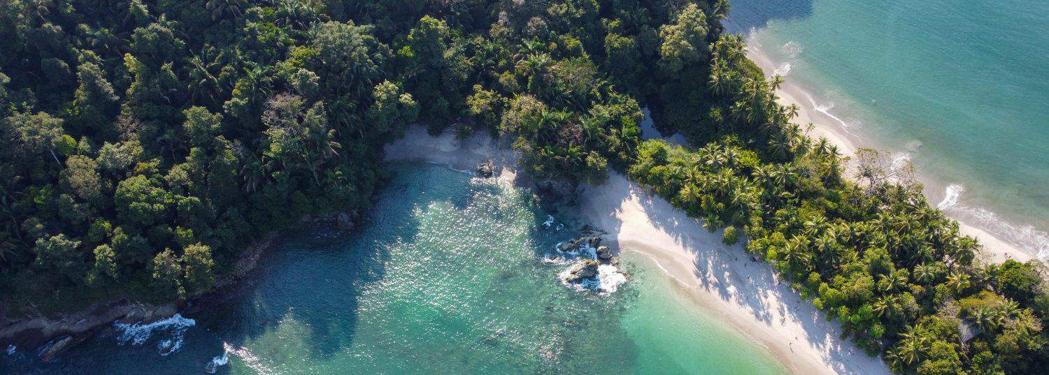 overhead shot of a white sand beach surrounded by lush green jungle and turquoise waters in costa rica