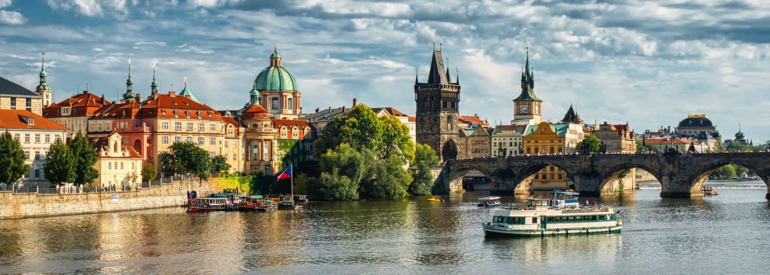 the beautiful old town of prague viewed from the river with a single boat passing by