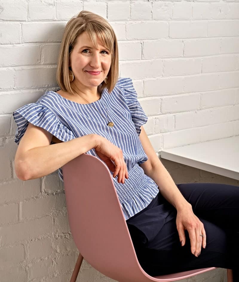 rebecca gade sawicki sitting in a pink chain against a white brick wall