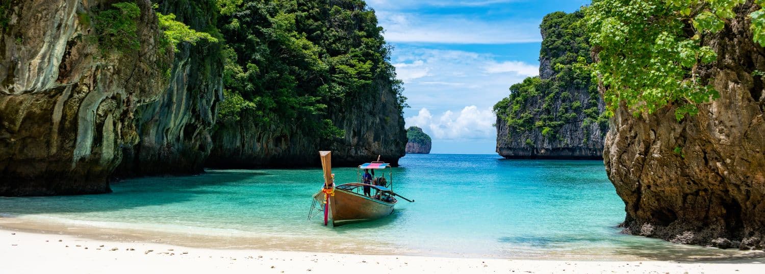 a secluded white sand beach in thailand with a single wooden boat sitting on the shore.