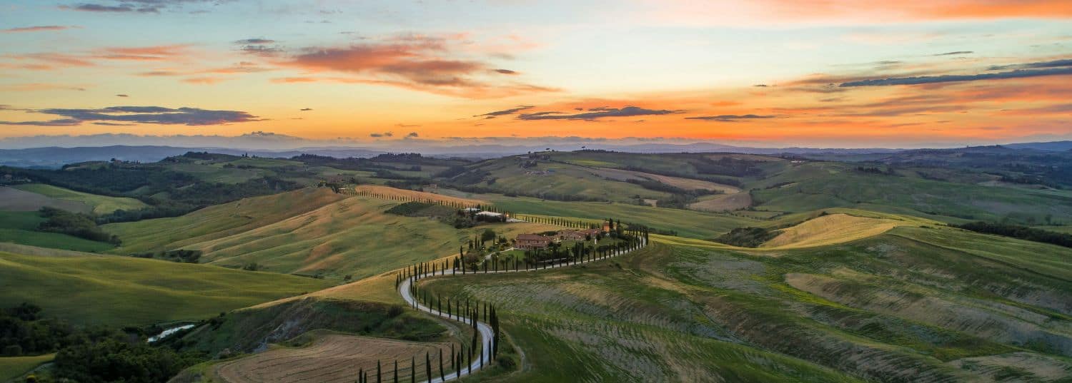 an orange and pink sunset over the green hills of tuscany