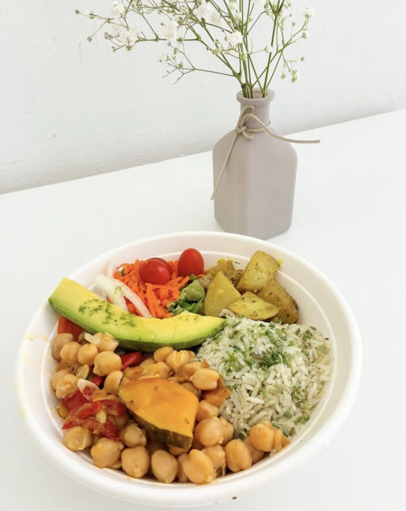 Vegan bowl with curry chickpeas, cilantro rice, potatoes, fresh salad, carrot and avocado. Next to flower vase. 