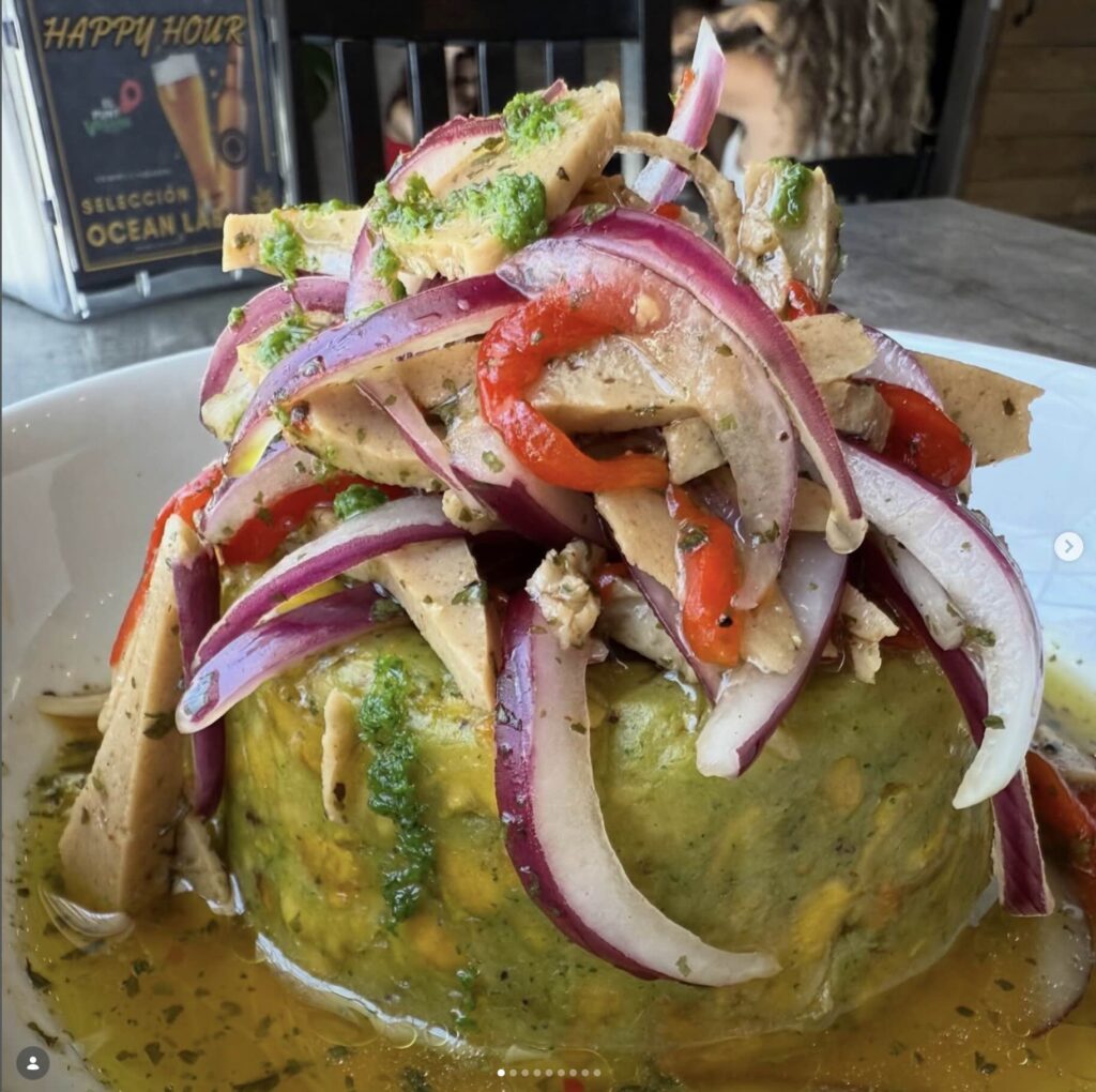 Vegan dish, guacamole based covered with seitan, purple onions, and bell peppers in white dish. 